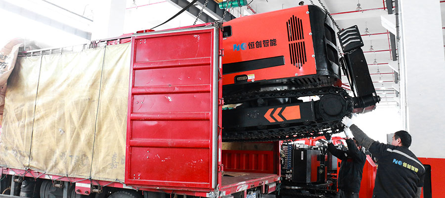 Workers use a forklift to load a large hydraulic demolition robot onto the back of a truck.