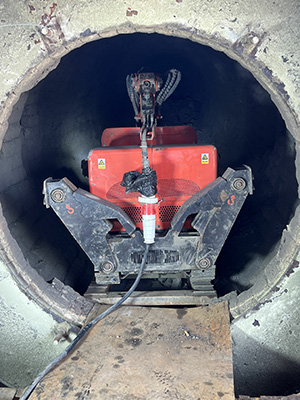 A worker using a remote control to precisely guide the HCR120D Demolition Robot as it demolishes inside an industrial kiln.